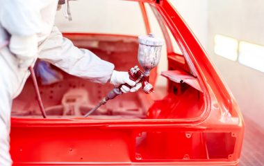 Close-up of spray paint gun with worker working on a red car